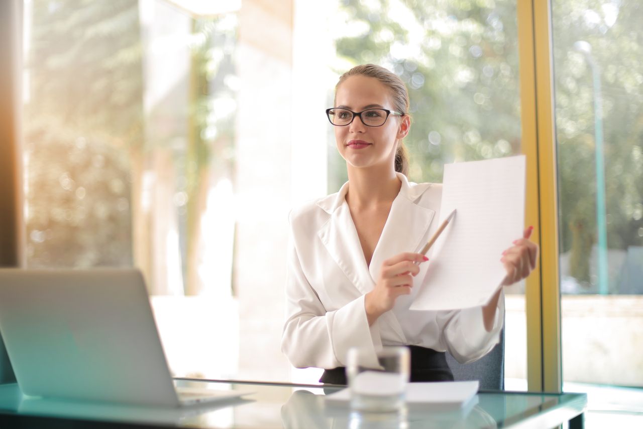 services-02 Young smart female entrepreneur wearing elegant jacket sitting at table in modern workplace and sharing business strategy while smiling and looking away