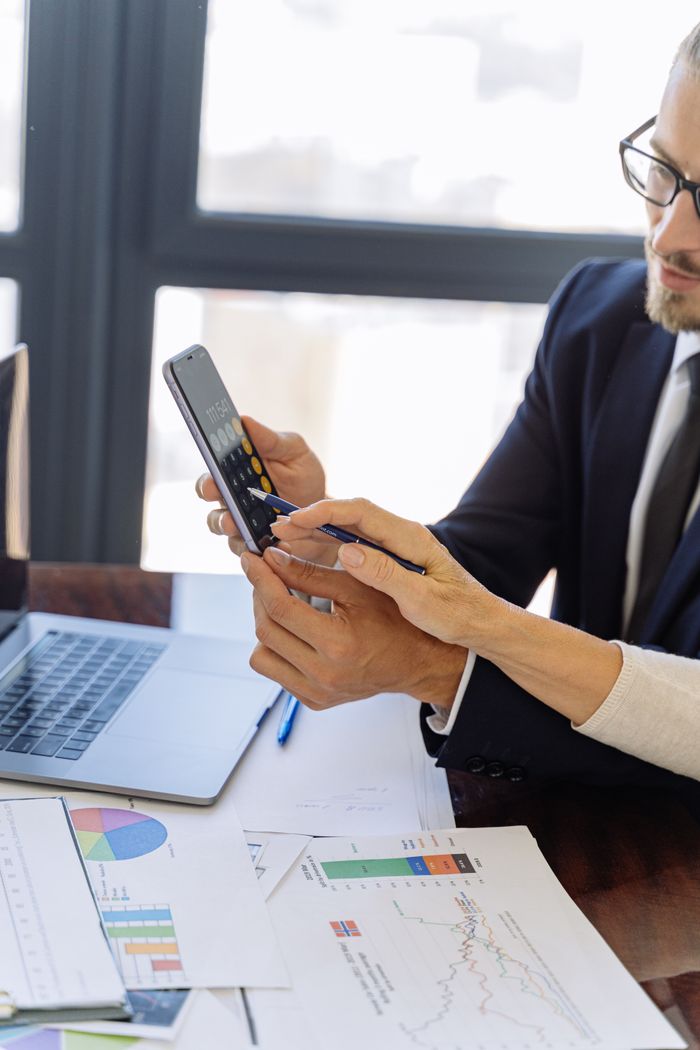 The Art of Drawing Readers In: Your attractive post title goes here Business professionals reviewing financial reports on a smartphone at a desk with papers and a laptop in an office setting.