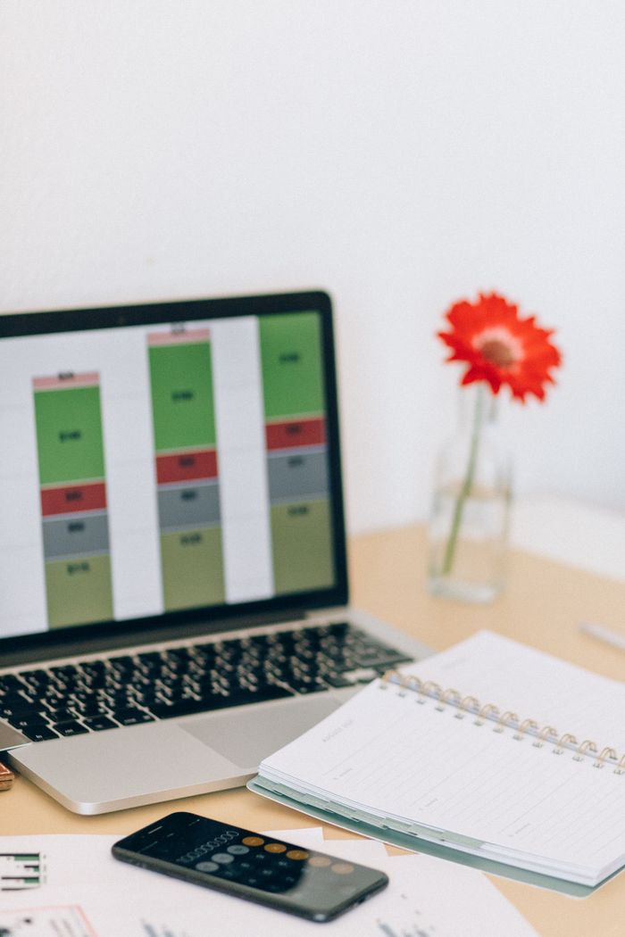A workspace featuring a laptop displaying graphs, calculator, notebook, and a red flower.